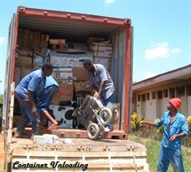 2 people unloading the container after it arrives in Muheza, one person stands to the side of the container, waiting to help