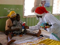 a person dressed in a santa hat gives children teddies, dontated to them by The Hereford-Muheza Link Society